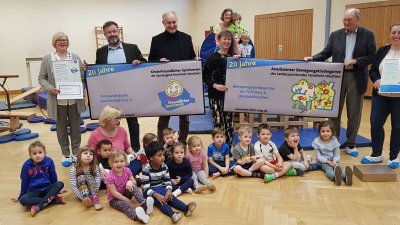 Gruppenfoto mit Staatssekretärin Andrea MIlz, vor ihr sitzen die Kinder der Eichhörnchen-Gruppe auf dem Turnhallenboden.