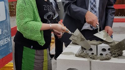 Staatssekretärin Andrea Milz spachtelt Mörtel zwischen die Mauersteine bei der Grundsteinlegung der Sporthalle Lüdinghausen.