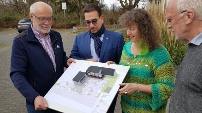 Staatssekretärin Milz (rechts) schaut sich mit drei Herren vom Badminton Club  einen Bauplan an. Sie stehen gemeinsam im Freien.