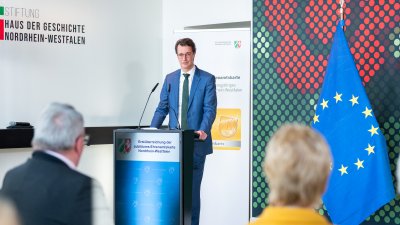 Hendrik Wüst spricht an einem Rednerpult vor einigen Menschen