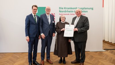 MP Wüst und Minister Lauman posieren mit Förderbescheidempfängern und eine Urkunde für ein Foto