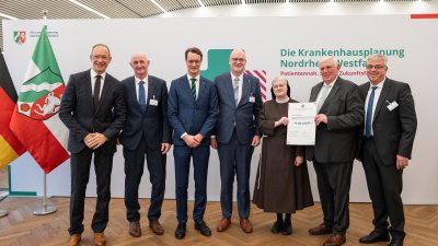 MP Wüst und Minister Lauman posieren mit Förderbescheidempfängern und eine Urkunde für ein Foto
