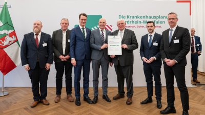 MP Wüst und Minister Lauman posieren mit Förderbescheidempfängern und eine Urkunde für ein Foto