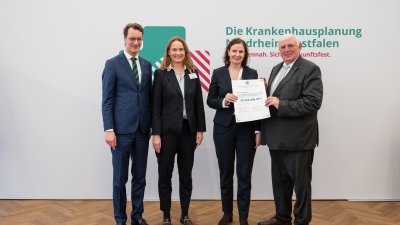 MP Wüst und Minister Lauman posieren mit Förderbescheidempfängern und eine Urkunde für ein Foto
