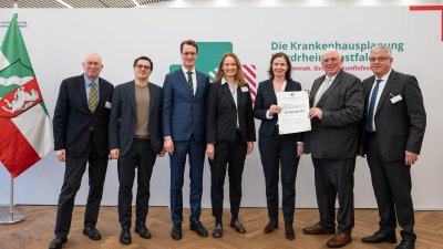 MP Wüst und Minister Lauman posieren mit Förderbescheidempfängern und eine Urkunde für ein Foto