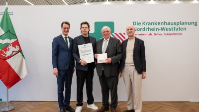 MP Wüst und Minister Lauman posieren mit Förderbescheidempfängern und eine Urkunde für ein Foto