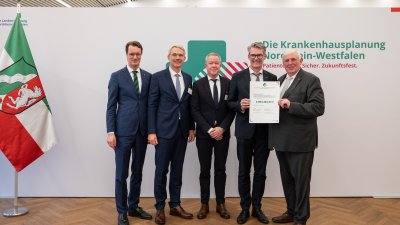 MP Wüst und Minister Lauman posieren mit Förderbescheidempfängern und eine Urkunde für ein Foto