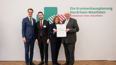 MP Wüst und Minister Lauman posieren mit Förderbescheidempfängern und eine Urkunde für ein Foto