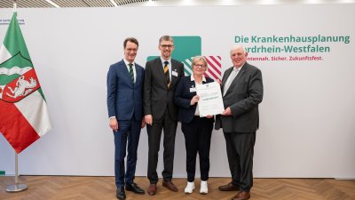 MP Wüst und Minister Lauman posieren mit Förderbescheidempfängern und eine Urkunde für ein Foto
