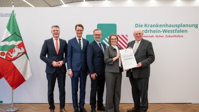 MP Wüst und Minister Lauman posieren mit Förderbescheidempfängern und eine Urkunde für ein Foto