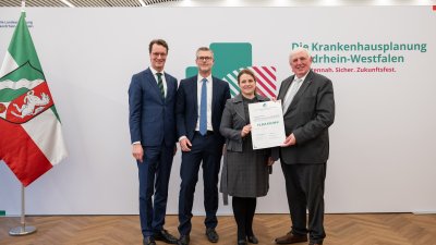 MP Wüst und Minister Lauman posieren mit Förderbescheidempfängern und eine Urkunde für ein Foto