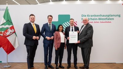 MP Wüst und Minister Lauman posieren mit Förderbescheidempfängern und eine Urkunde für ein Foto