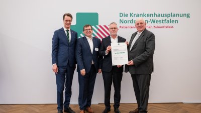 MP Wüst und Minister Lauman posieren mit Förderbescheidempfängern und eine Urkunde für ein Foto