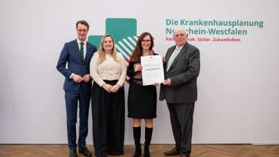 MP Wüst und Minister Lauman posieren mit Förderbescheidempfängern und eine Urkunde für ein Foto