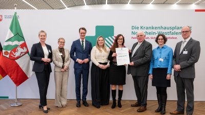 MP Wüst und Minister Lauman posieren mit Förderbescheidempfängern und eine Urkunde für ein Foto