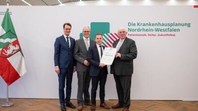 MP Wüst und Minister Lauman posieren mit Förderbescheidempfängern und eine Urkunde für ein Foto