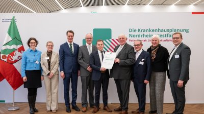 MP Wüst und Minister Lauman posieren mit Förderbescheidempfängern und eine Urkunde für ein Foto