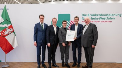 MP Wüst und Minister Lauman posieren mit Förderbescheidempfängern und eine Urkunde für ein Foto