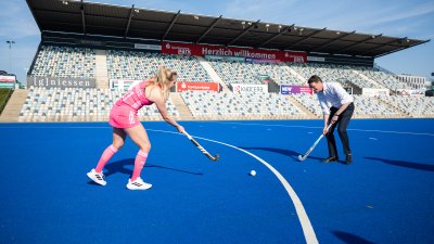 MP Wüst und eine Hockey-Spielerin spielen auf einem blauen Stadionplatz