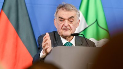 Minister Reul spricht an einem Rednerpult vor Flaggen