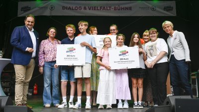 Ministerin Feller und eine Schulgruppe posieren für ein Foto auf einer Bühne