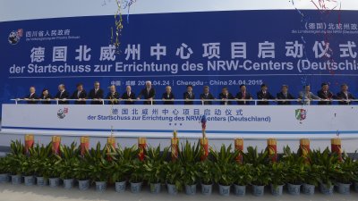 Viele Teilnehmer halten ein Geländer vor einer großen Plakatwand mit dem Titel der Veranstaltung