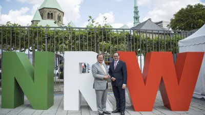 Herr Laschet und Herr Kufen stehen vor großen NRW-Buchstaben