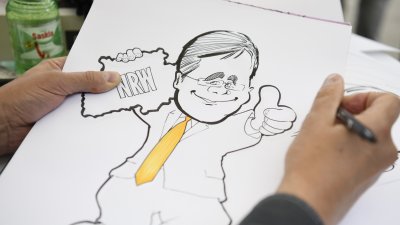 Ein Karikaturist zeichnet Ministerpräsident Armin Laschet mit gelber Krawatte und gehobenem Daumen