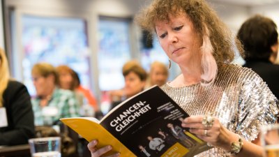 Staatssekretärin für Sport und Ehrenamt Andrea Milz sitzt in der Frauen-Vollversammlung und schaut in ein Magazin namens Chancen-Gleichheit.