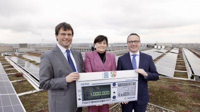 Drei Personen stehen auf einem Dach vor einer großen Solar-Anlage und halten gemeinsam einen Scheck hoch