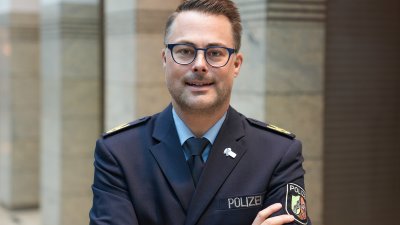 Ein Mann mit kurzen Haaren und Brille in Polizeiuniform und verschränkten Armen schaut lächeld in die Kamera