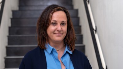 Porträtfoto einer Frau mit braunen Haaren und blauer Bluse vor einer Treppe