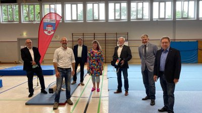 Staatssekretärin Andrea Milz steht mit mehreren Vereinsmitgliedern in einer Turnhalle, überall sidn verstreut Matten auf dem Boden verteilt.