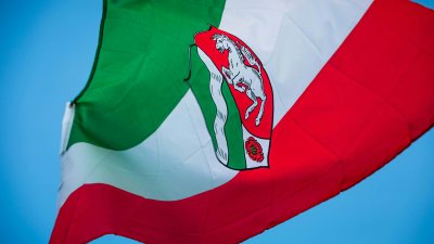 die Flagge Nordrhein-Westfalens weht im Wind, zu sehen sind die Landesfarben grün, weiß, rot sowie das Landeswappen in der Mitte der Flagge