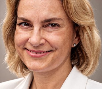 Eine blonde Frau in weißem Blazer lächelt in die Kamera