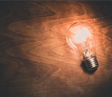 Auf einer Tischplatte liegt eine einzelne, leuchtende Glühlampe