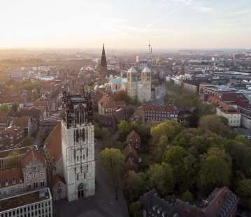 Blick von oben auf Münsters Altstadt: Im Vordergrund steht die Überwasserkirche, dahinter ist der Dom mit seinen beiden Türmen und die Lambertikirche zu sehen. Am Horizont erkennt man Münsters höchstes Bauwerk, den Fernsehturm. 
