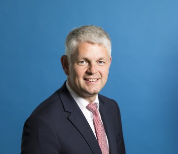 Staatssekretär Dammermann freundlich lächelnd - Hintergrund blau.