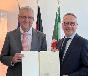 Minister Dr. Limbach rechts im schwarzen Anzug übergibt Klaus Georg Müller im grauen Anzug mit roter Krawatte eine Urkunde