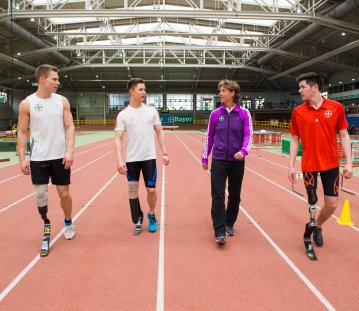 4 Sportler auf einer roten Tartanbahn. 3 von ihnen haben je eine Beinprothese.