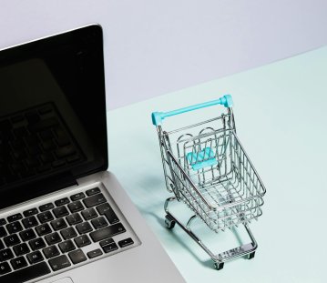 Neben einem Laptop steht ein Miniatur-Einkaufswagen