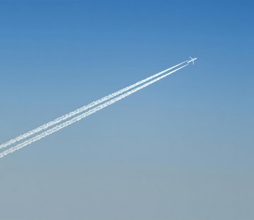 Flugzeug hoch oben am blauen Himmel, mit Kondesstreifen hinter sich