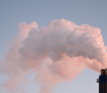 Rauch, der aus einem Industrieschornstein gegen einen klaren Himmel aufsteigt und die Verschmutzung veranschaulicht.