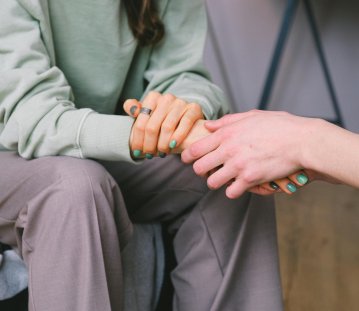 Zwei Frauen halten sich an den Händen, ihre Köpfe sind nicht zu sehen