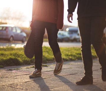 Zwei Personen gehen neben einer Straße auf dem Gehweg