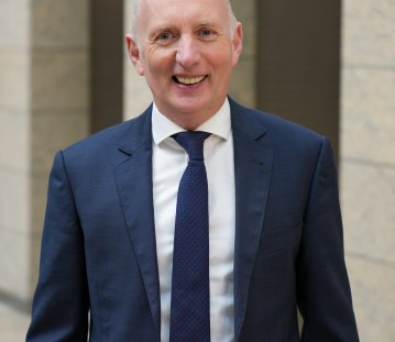 ein Mann in blauem Anzug, weißem Hemd und blauer Krawatte lächelt