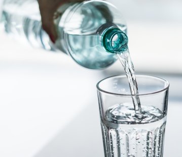 Eine Hand gießt aus einer Flasche Wasser in ein Glas.