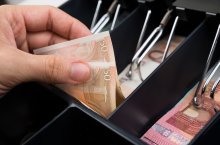 Jemand nimmt mit seiner linken Hand einen 50 Euro-Schein aus einer Kasse.
