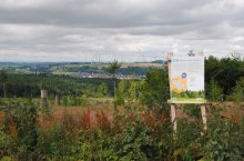 Eine Hinweistafel steht auf einem Hügel an einem Waldrand mit Ausblick in die Ferne