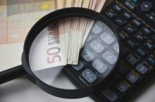 Geld und Taschenrechner liegen unter der Lupe